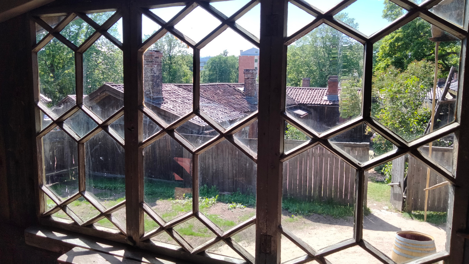 Kuvassa on ikkuna, jossa soikean muotoista koristeristikkoa. Ikkunasta näkyy harmaita museon rakennuksia.