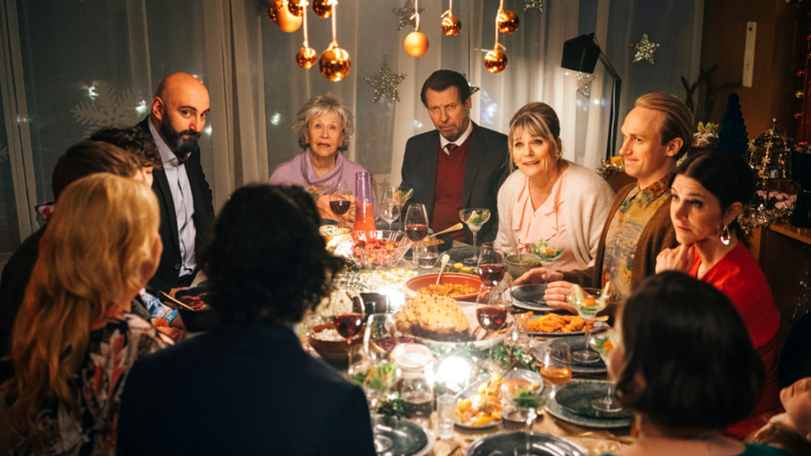 Kuvassa ovat elokuvan näyttelijät joulupöydän ympärillä keskustelemassa iloisesti ja pöydässä on ruokaa. 