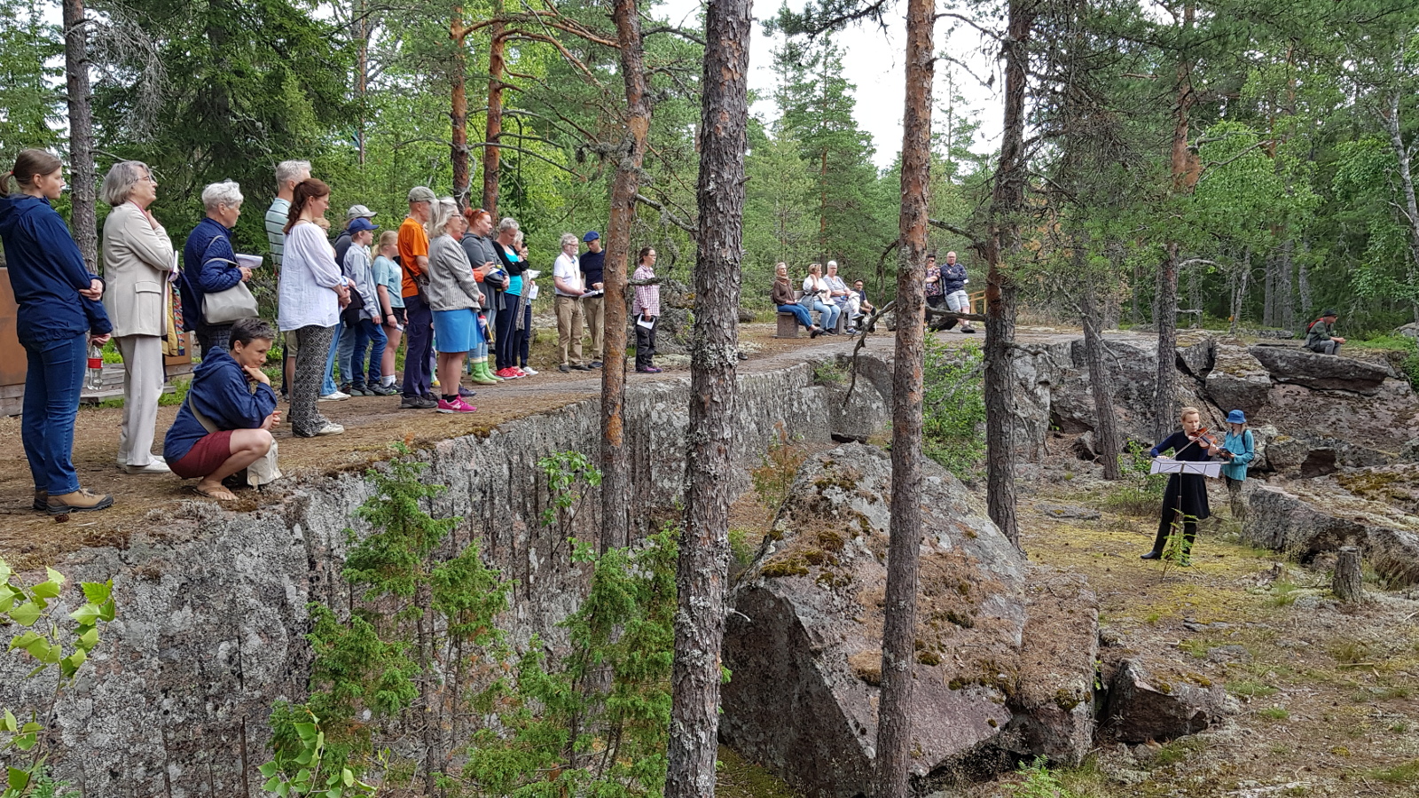 Kuvassa ovat oikealla alhaalla Pyterlahden louhistossa Viola Räisänen soittamassa viulua ja hänen takanaan Anni Kivimäki lukemassa tekstiään. Ylempänä pystysuoran kallion päällä on yleisöä nauhana kallion päällä.