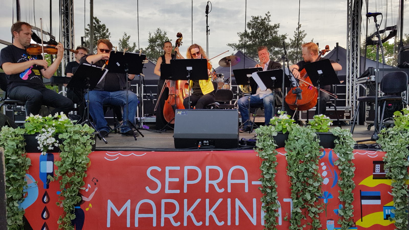 Kuvassa Kaakon Kamarimusiikin Tangoyhtye ulkoilmalavalla. Alla on punapohjaisella lakanalla keltaisella teksti Sepramarkkinat.