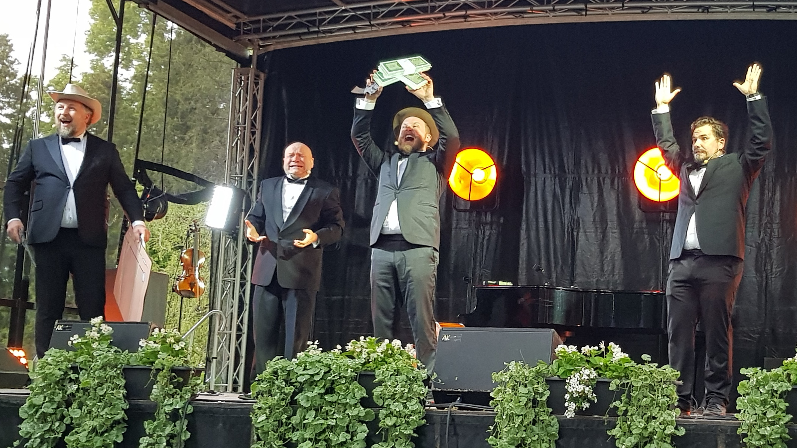 Kuvassa ovat Uuden Kipparikvartetin laulajat ja vasemmalla Tuukka Haapaniemellä on päässään stetson ja kädessään pahvinen matkalaukku. Taaempana Petri Bäckström ja etualalla Sampo Haapaniemi kädessään ylhäällä isoja dollarin seteleitä.  Oikealla Jouni Bäckström kädet ylhäällä.