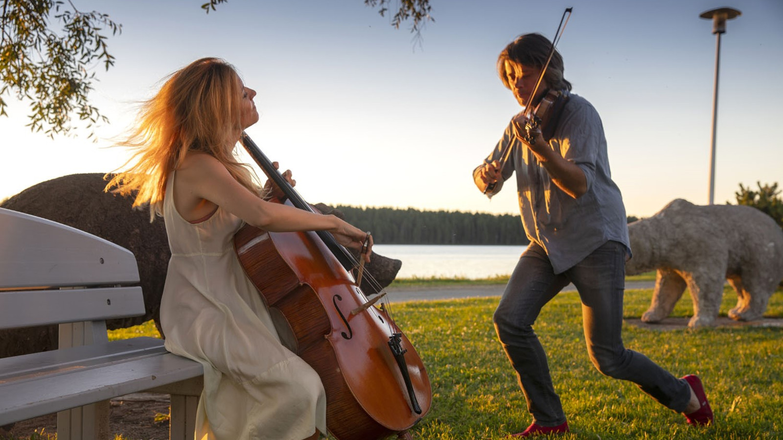 Kuvassa ovat Daniel Rowland soittamassa selloa ja Maja Bogdanovic viulua nurmikolla ja aurinko heijastuu vasemmalta kesäillassa.