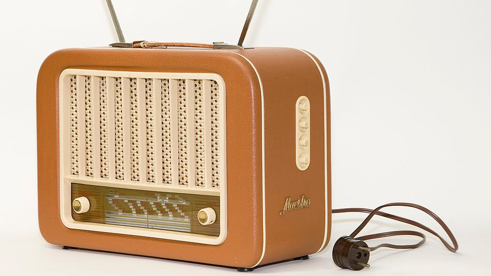 Kuvassa on vanhanaikainen hiukan kulmikas vaalean ruskea radio ja sen töpseli on irrallaan vieressä.