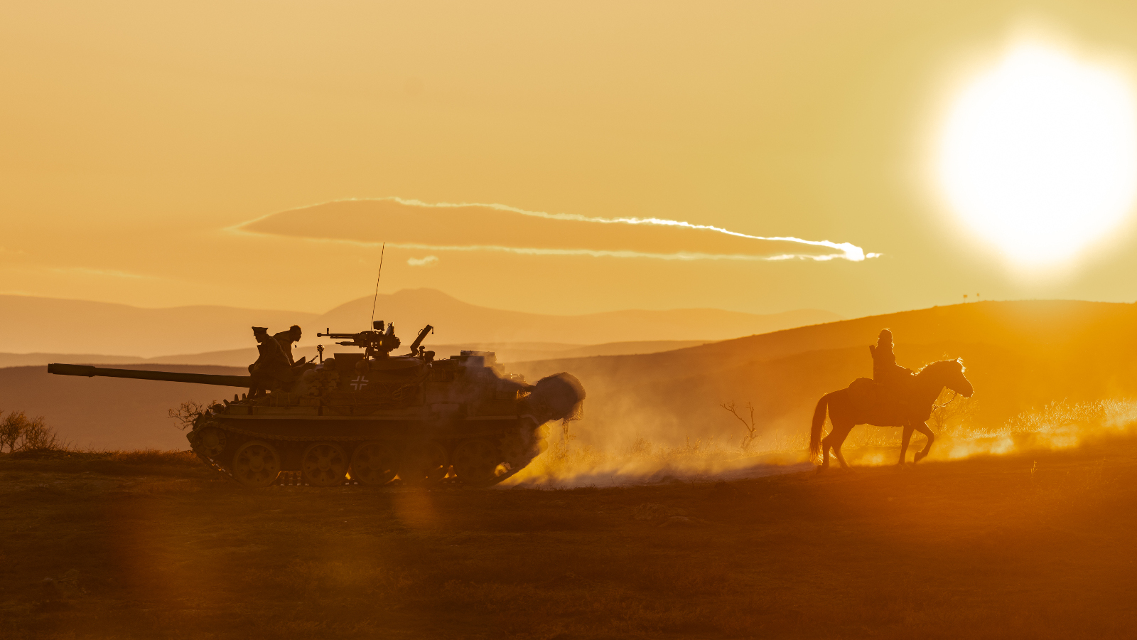 Kuvassa on ruskean kellertävän taivaan loisteessa edellä menevän hevosen ja ratsastajan takana panssarivaunu.  