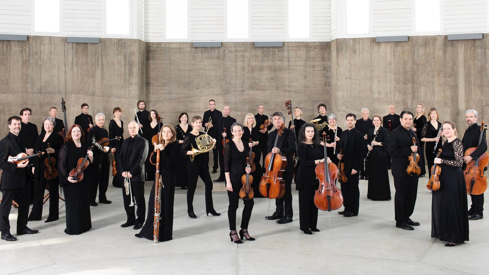 Kuvassa on orkesterin St. Martin in the Fields jäsenet seisomassa soittimet kädessään ja seisovat.  Taustalla on harmaa seinä. 