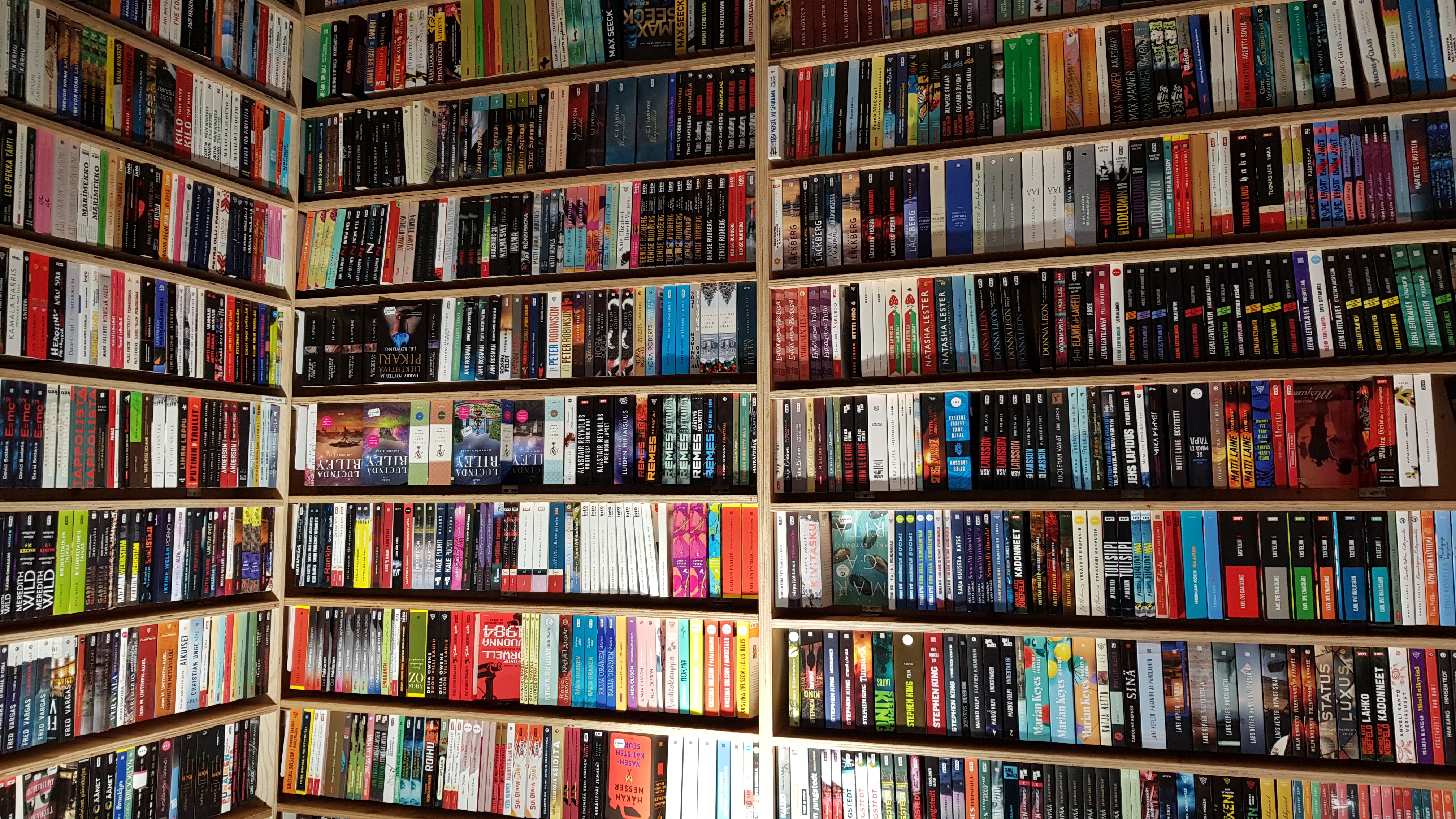 Kirjoja kirjakaupan hyllyssä ja hyllyt tekevät kulman.  Hyllyjä ja kirjoja on koko kuva-alalla.