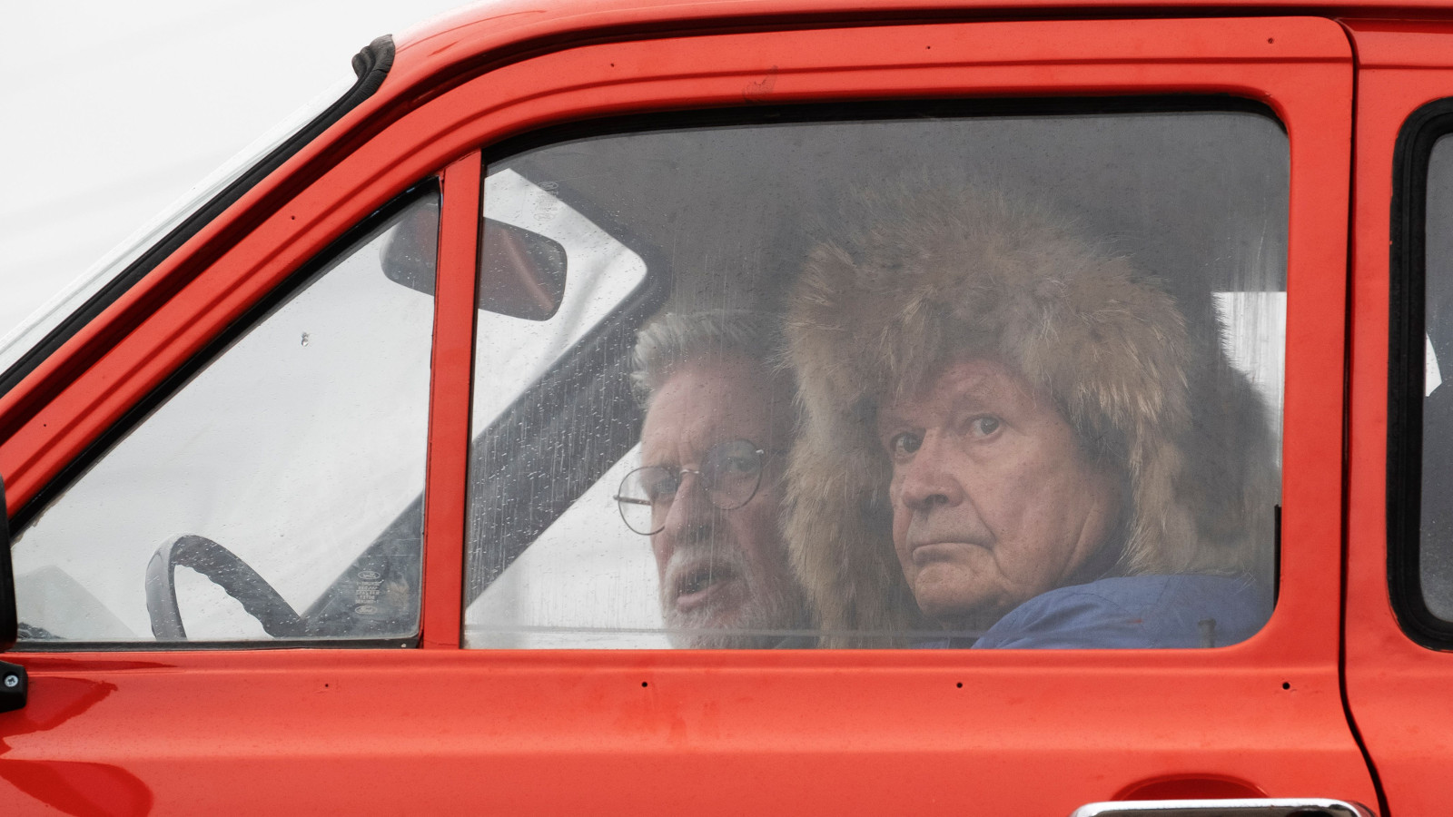 Kuvassa on punaisen Escortin ikkuna, josta näkyy Heikki Kinnusen pää karvahattu päässä.  Takana näkyy Kari Väänänen.