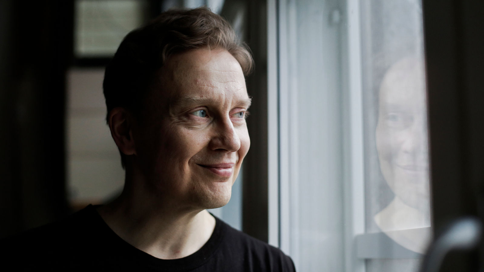 Kuvassa on Teemu Mäki, joka katsoo sivuun lasin läpi.  Lasista heijastuvat hänen kasvonsa.