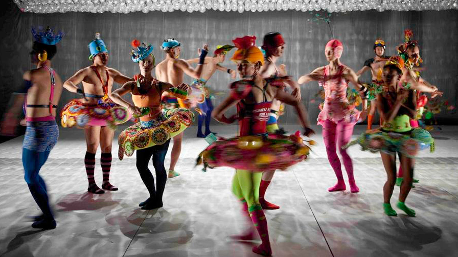 Kuvassa on balettitanssijoita värikkäissä ja erilaisissa asuissa, useimmat klassisen balettiasun tyyppisessä kirjavassa asussa lavalla tanssimassa.