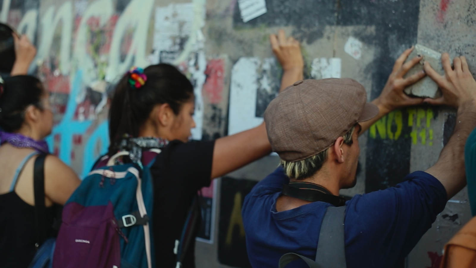 Kuvassa on selin nuori tyttö ja poika etualalla laittamassa lappuja seinämuuriin, jossa on paljon viestejä ja lisäksi graffiteja.