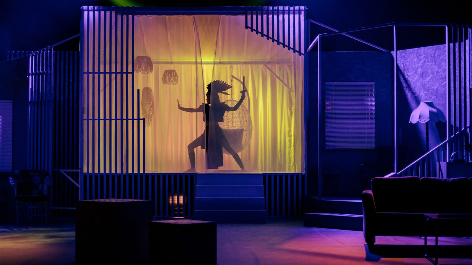 Kuvassa on sinertävää valoa olohuoneessa ja taustalla näkyy heijastettu soturihahmo tanssiasennossa.