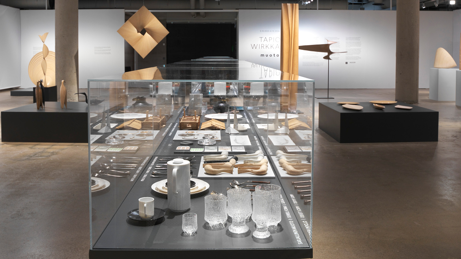 Kuvassa on Wirkkalan näyttelyhuone, jossa on keskellä vitriini ja näyttelyesineitä.  Seinillä on myös ripustettuna mm. puusta muotoiltuja esineitä.