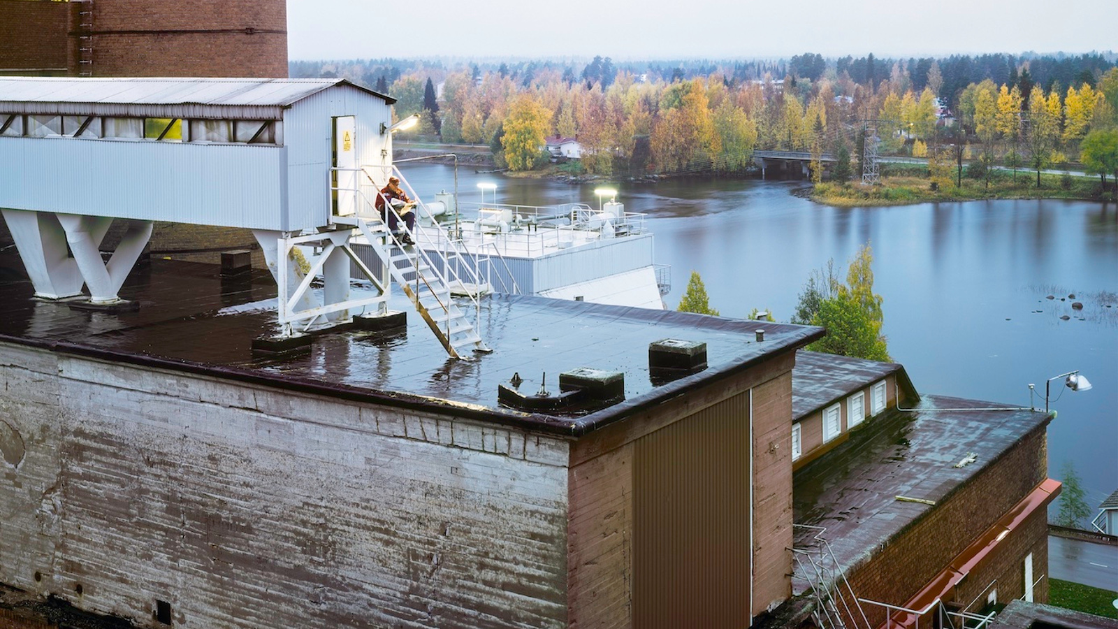 Kuvassa on proomu, jonka kannella on mies juomassa aamukahvia.  Proomu on valkoinen ja veden takana näkyy kaupungin silhuettia.