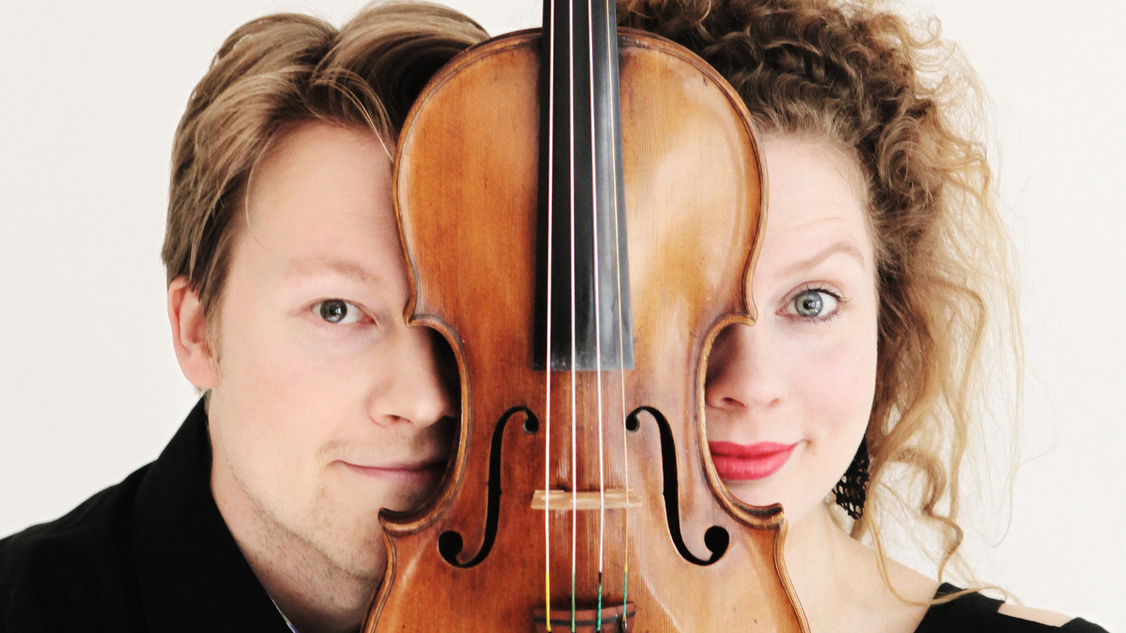 Kuvassa ovat Antti Tikkanen ja Minna Pensola. Kuvan keskellä on viulu ja sen molemmin puolin näkyy heidän kasvoistaan puolet.