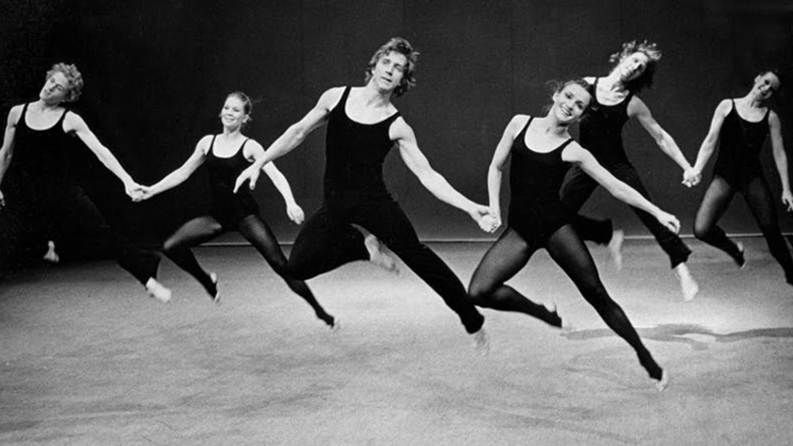 Kuvassa on kuusi tanssijaa ilmahypyssä, jossa he ovat jalat vinosti ylhäällä ja kaksittain käsi kädessä. Kuva on musta-valkoinen.