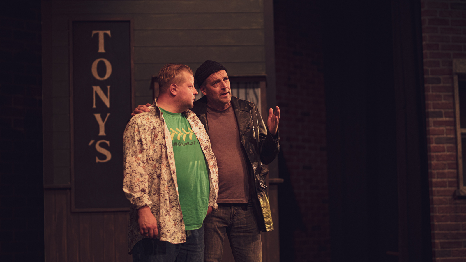 Kuvassa on kaksi miestä keskustelemassa ja taustalla näkyy ylhäältä alaspäin teksti Tony's.  Toisella miehistä on vaalean vihreä t-paita.