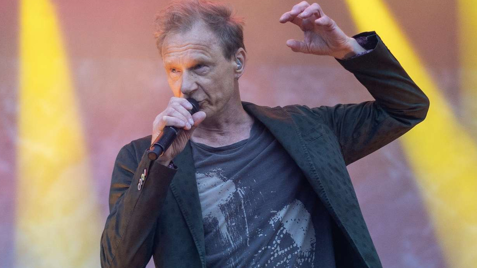 Kuvassa on Ismo Alanko laulamassa mikkiin etuviistosta kuvattuna ja toinen käsi puoliksi ylhäällä. Tausta on vaalean violetti ja siinä on kaksi keltaista pystysuoraa valoraitaa.