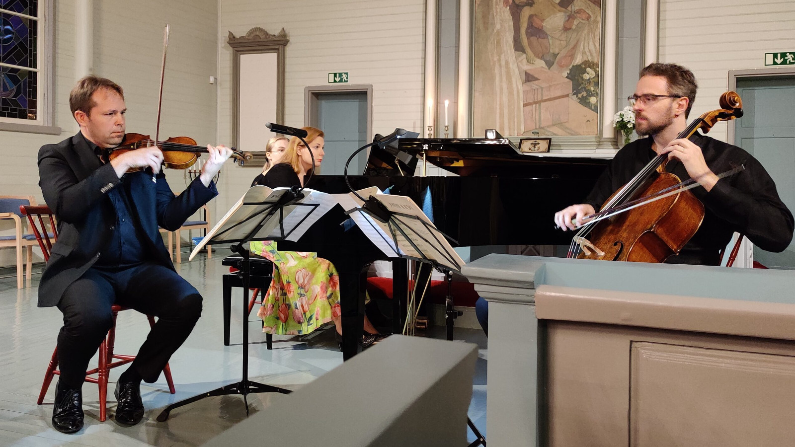 Kuvassa ovat Jukka Merjanen viulussa ja Tuomas Ylinen sellossa etualalla Virolahden kirkon alttarilla sekä takana Liisa Malmivaara flyygelissä.