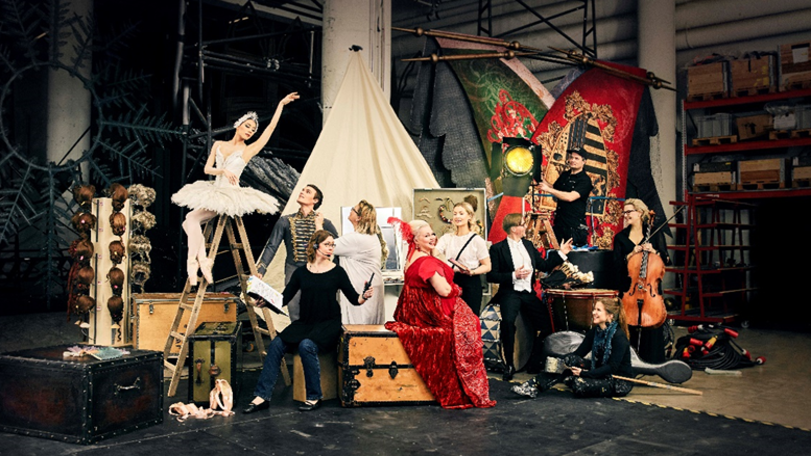 Kuvassa on oopperan ja baletin esiintyjiä erilaisissa puvuissa rekvisiitan keskellä.