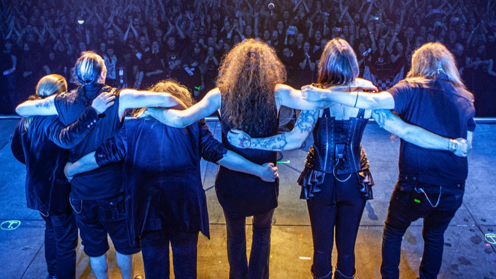Kuvassa ovat Nightwishin jäsenet seisomassa yleisön edessä Wembleyn stadionilla yleisön edessä yhteiskuvassa. Kuvan sävy on sininen.