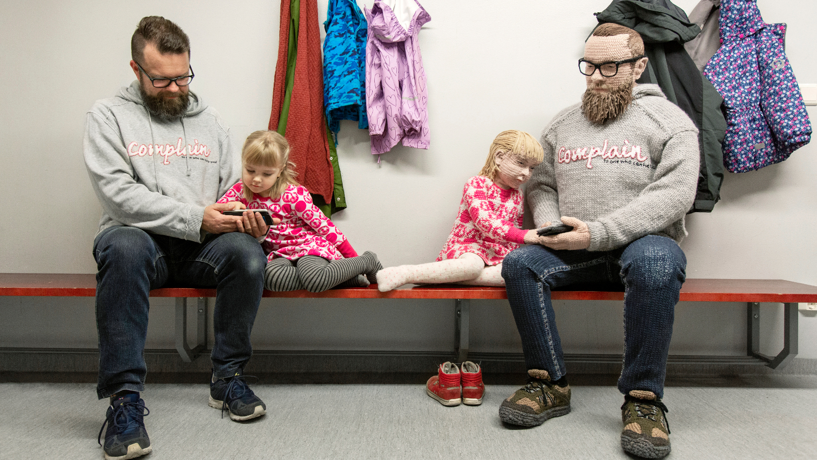 Kuvasssa on penkillä istumassa vasemmalla isä ja noin 3-vuotias vaaleatukkainen tytär. Heistä on vieressä identtiset virkatut hahmot istumassa penkillä.
