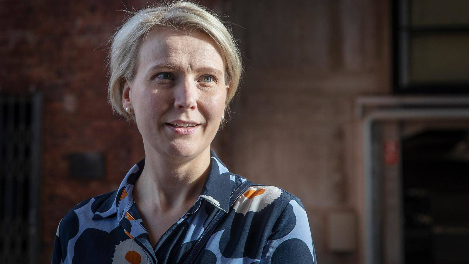 Kuvassa on Mirja Mäen kasvokuva ja hänellä on vaaleat hiukset sekä sinikukkainen Marimekon Unikko-kuvioinen paita päällään.