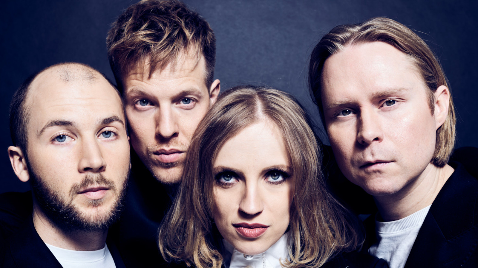 Kuvassa ovat Haloo Helsinki! bändin neljä jäsentä tiiviissä ryhmäkuvassa, jossa näkyvät vain kasvot.