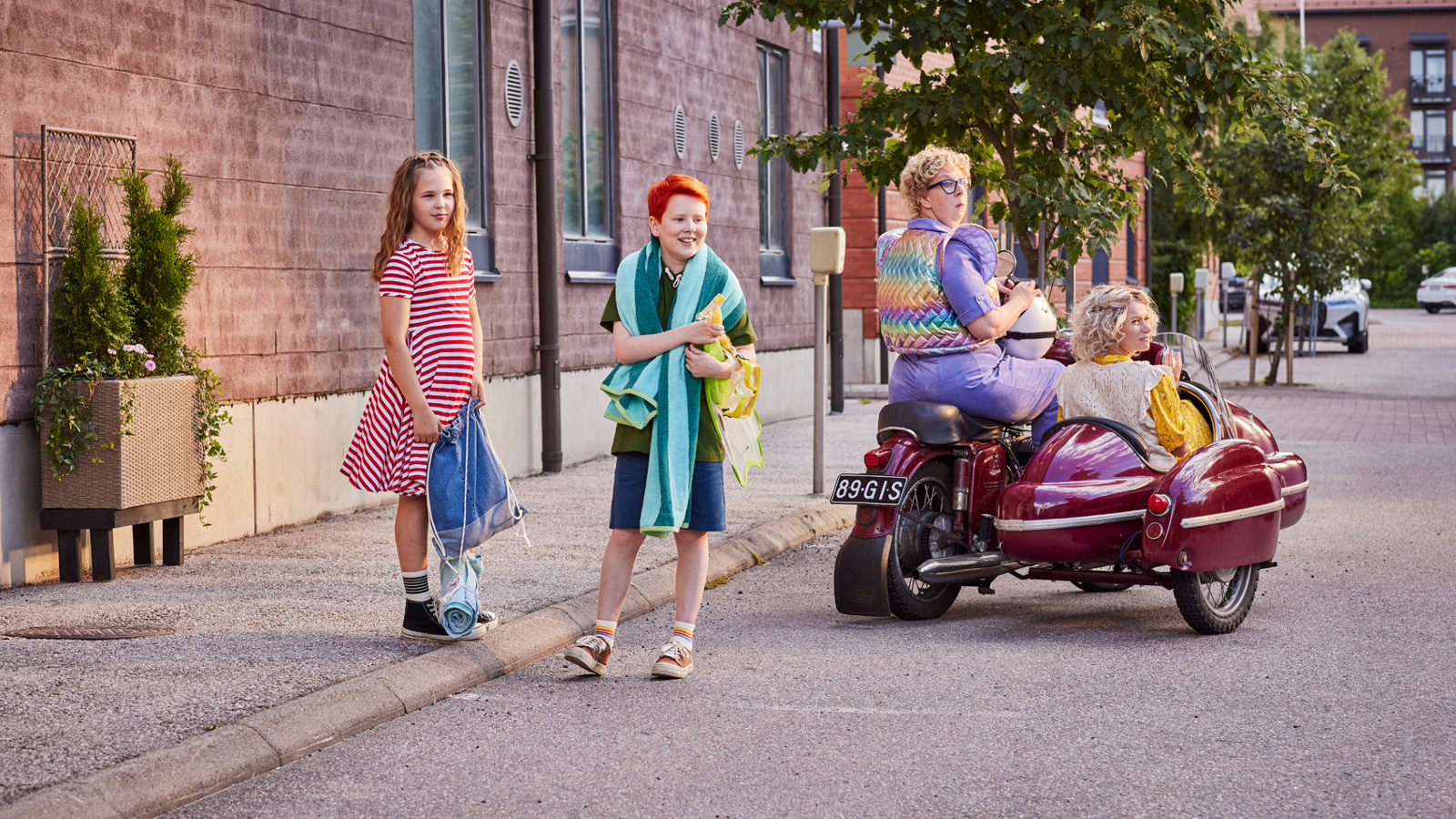 Kuvassa ovat vasemmalla seisomassa kadulla Nelli Nuudelipää sini-valkoraidallisessa mekossa ja Risto Räppääjä shortseissa ja t-paidassa.  Vieressä ovat moottoripyörän päällä Pakasta-Elvi ja punaisessa sivuvaunussa Rauha Räppääjä.