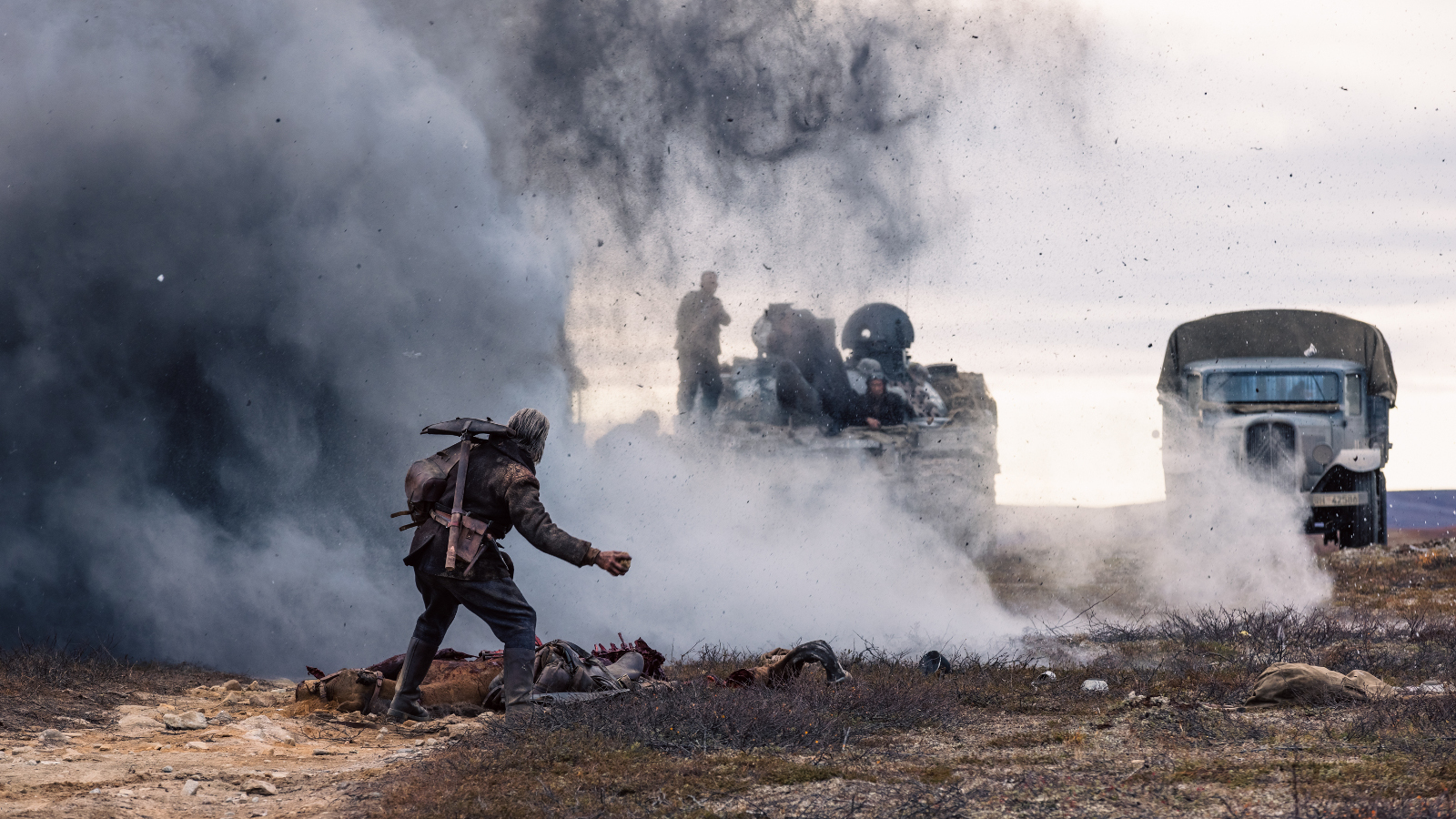 Kuvassa on etualalla kumarassa kulkeva Jorma Tommila ja hänen edessään on savua ja panssarivaunu miehistöineen. Oikealla on miehistönkuljetusauto.