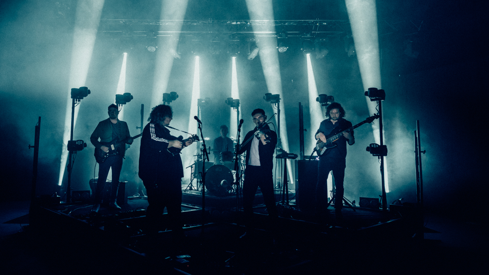 Kuvassa on Elephant Sessions -yhtyeen viisi jäsentä esiintumässä sinertävällä esiintymislavalla, jossa on voimakkaita pystysuoria valoja.  Kuvan alaosa on tumma.
