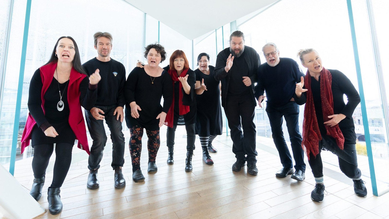 Kuvassa on Iki-Turson kahdeksan soittajaa, jotka ovat iloisilla ilmeillä hiukan eteenpäin kumartuneina valoisan konserttisalin aulatilassa.