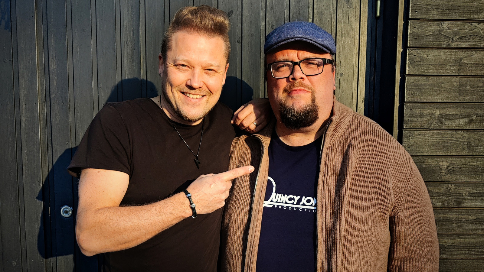 Kuvassa ovat Tomi Salesvuo  mustassa t-paidassa vasemmalla ja Sami Pitkämö pusakassa oikealla seisomassa ulkona.  Kuva on puolivartalokuva. 