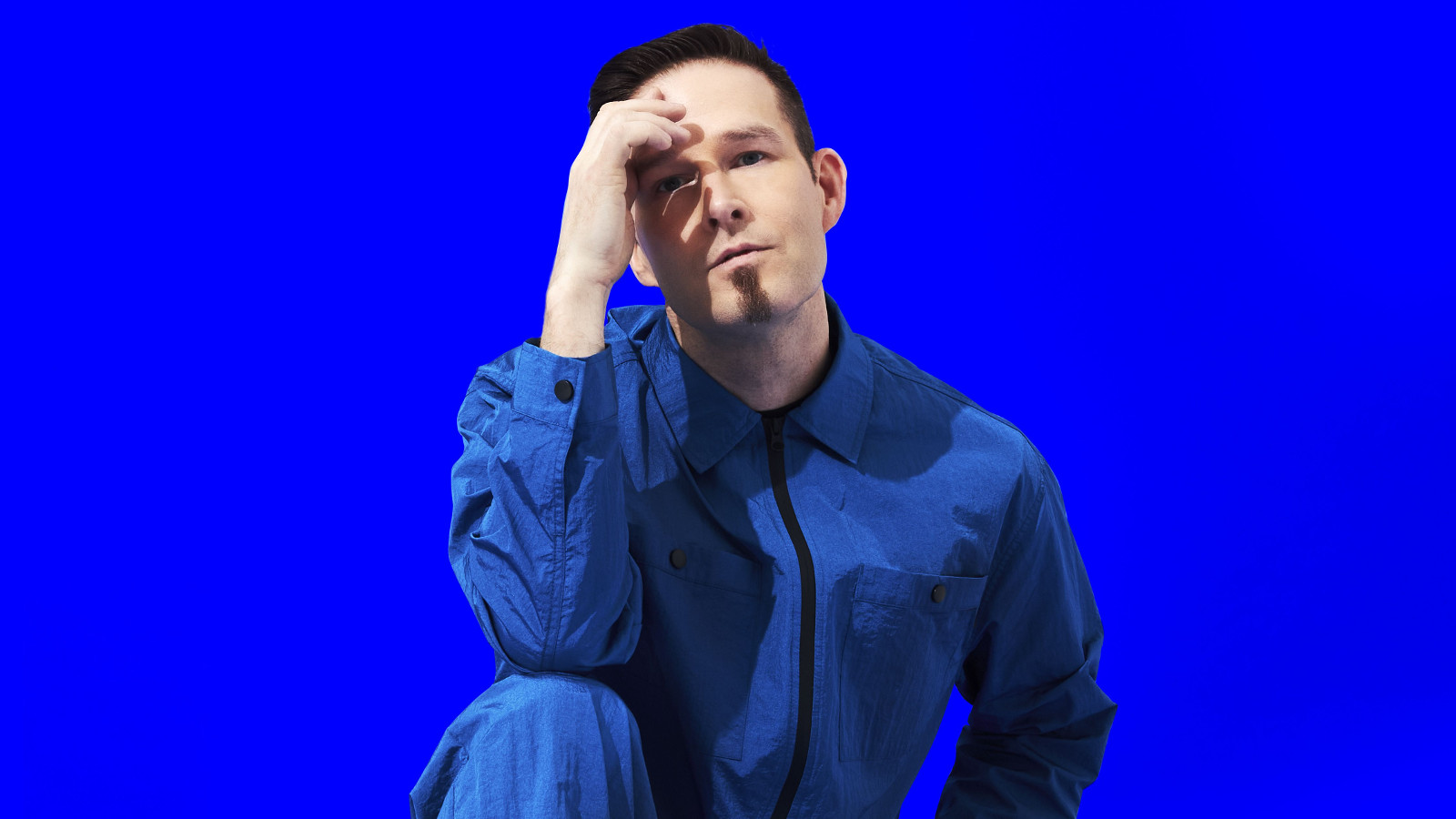 Kuvassa on Darude, joka nojaa kyykkyasennossa oikealla kädellään ohimoonsa.  Tausta on kirkkaan sininen.