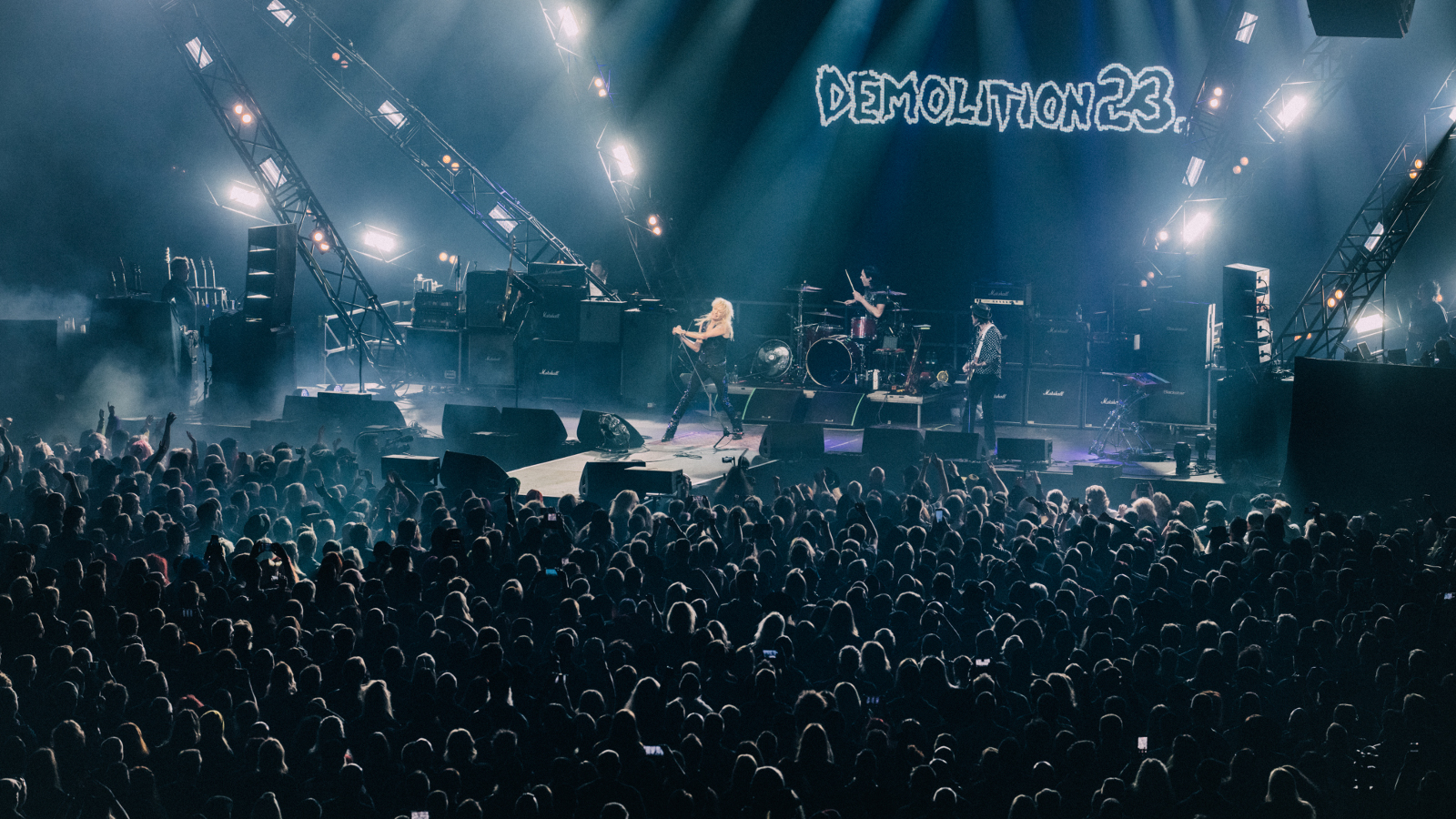 Kuvassa on lavalla esiintymässä Michael Monroe Demolition 23 -yhtyeen kanssa ja nimi on isolla taustalla. Etualalla on yleisöä.  Kuvan sävy on sininen.
