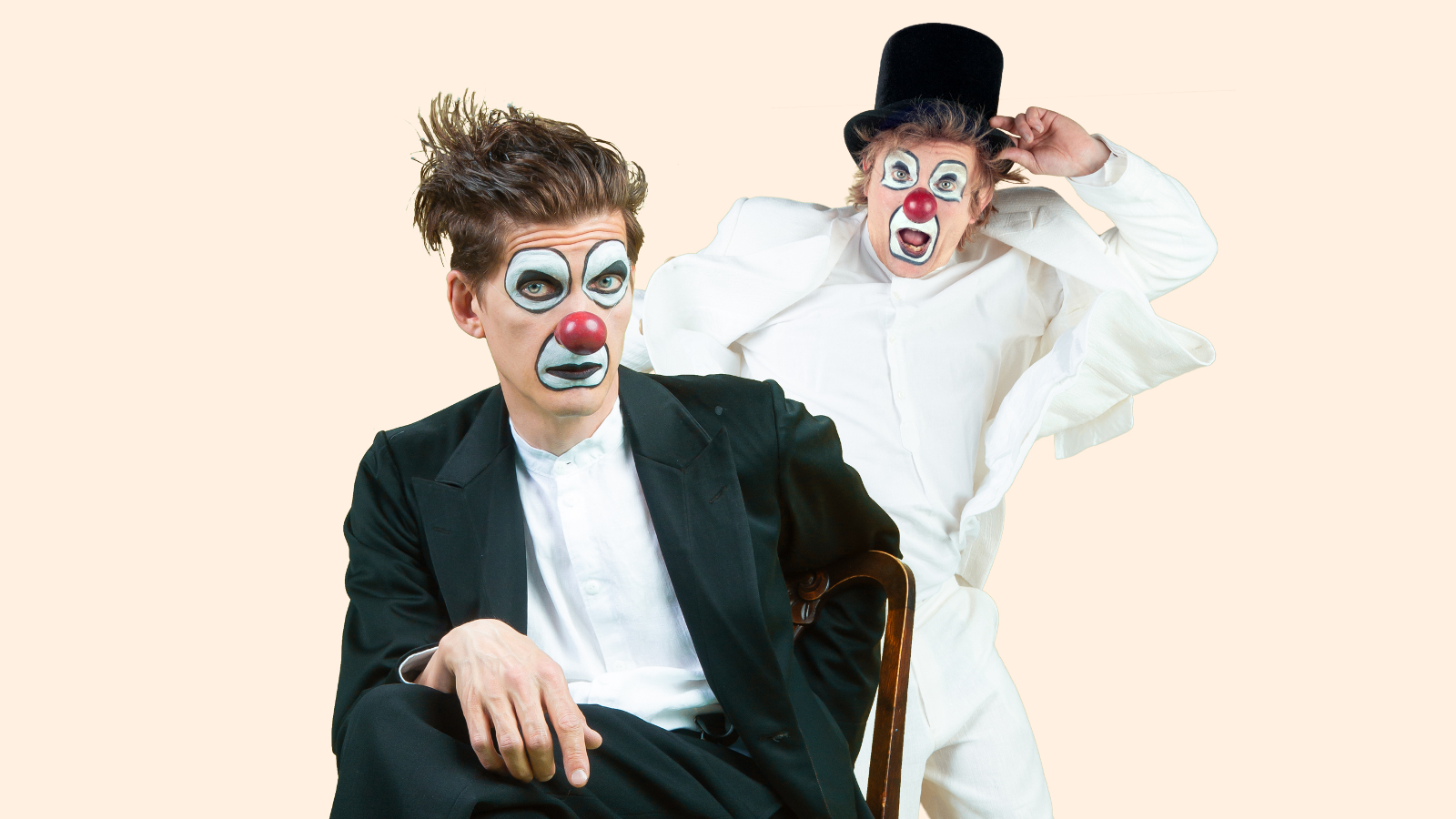 Kuvassa on etualalla Timo Ruuskanen sirkusmaisessa maskissa istumassa mustassa puvussa ja takana Tuukka Vasama vastaavalla maskilla ja vaaleassa asussa.