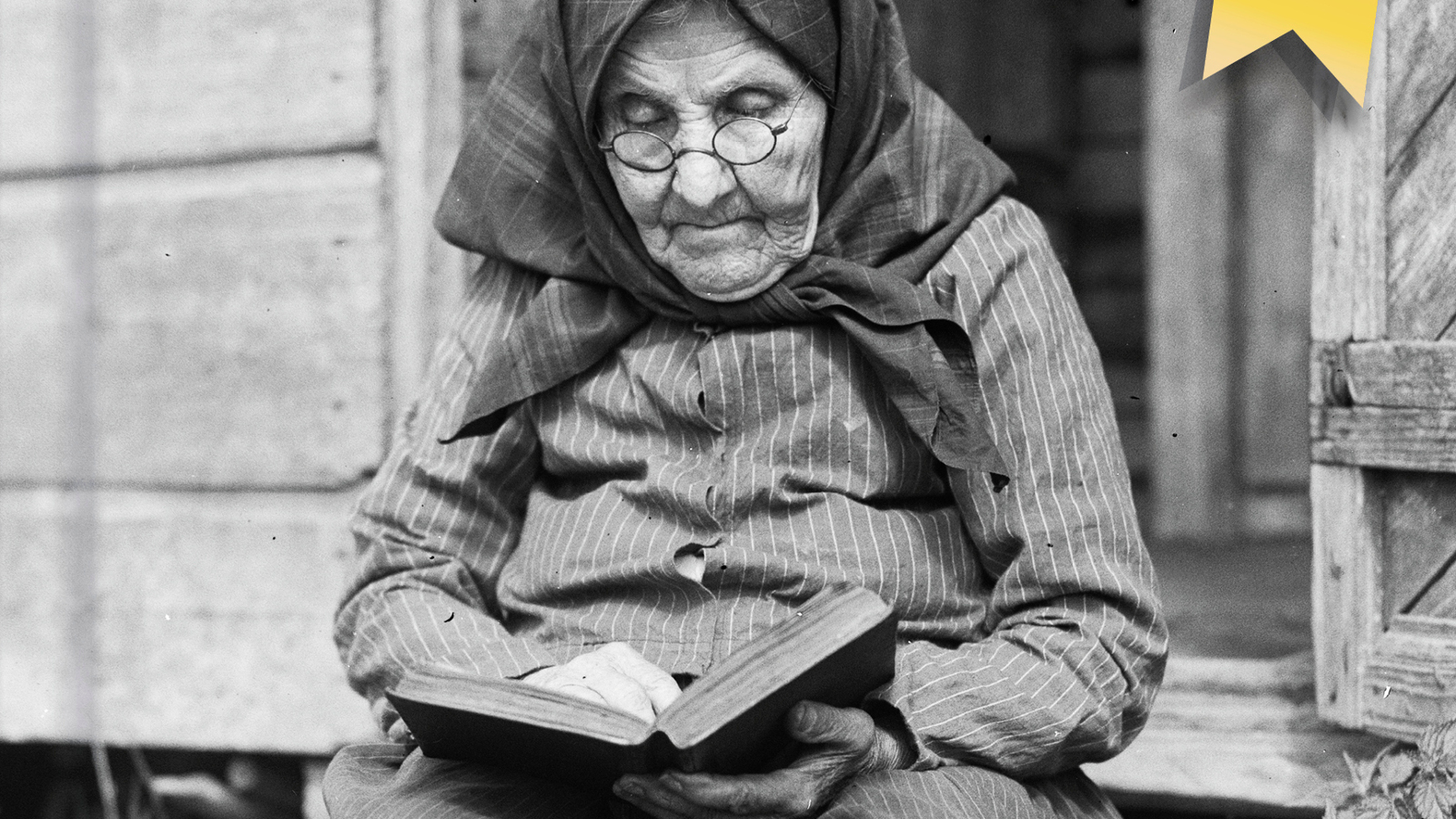 Kuvassa on vanha, ryppyinen nainen musta huivi päässään lukemassa kirjaa. Hän istuu portailla. Kuva on musta-valkoinen.