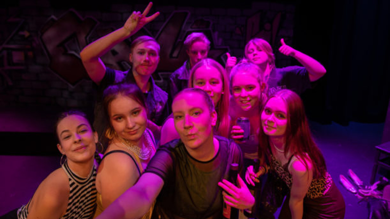 Kuvassa ovat näytelmän nuoret esiintyjät ryhmäkuvassa ja heihin kohdistuu violettia valoa.