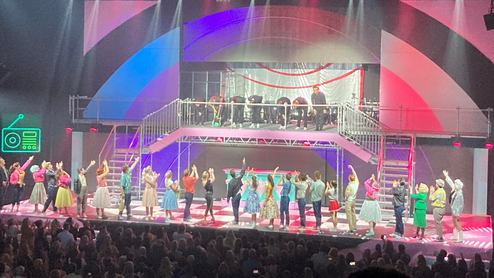 Kuvassa ovat lavalla kaikki esiintyjät nauhana lavalla. Taustalla näkyy lavasteet, joissa on neliömäisessä taulussa sinisiä, punaisia ja mustia paksuja kaaria.