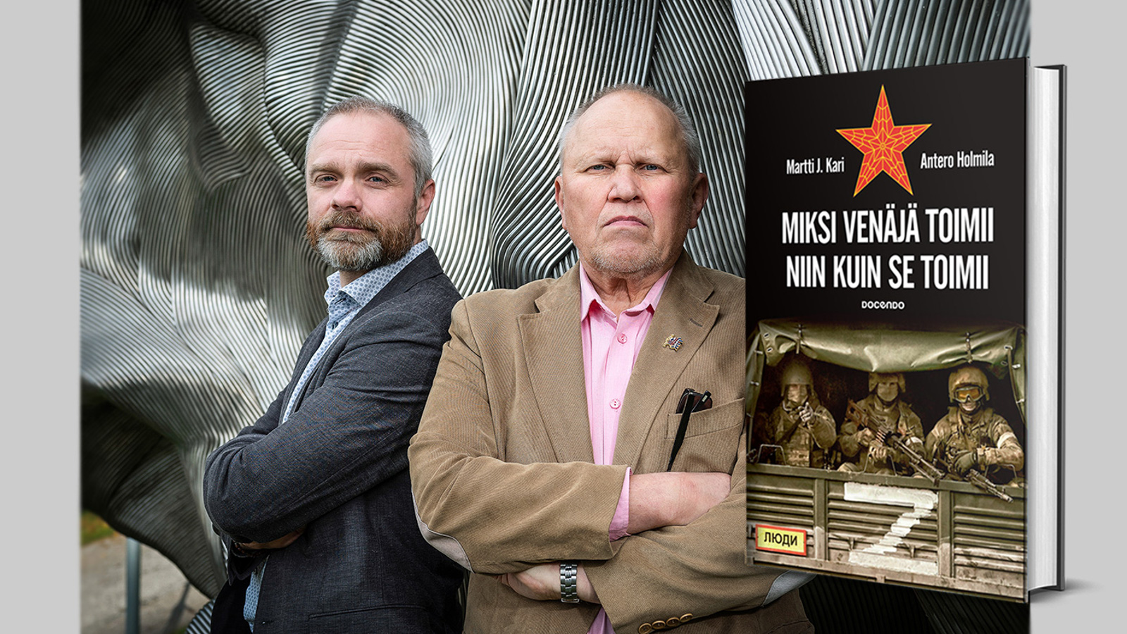 Kuvassa ovat Antero Holmila tumman harmaassa takissa ja Martti J. Kari vaalean ruskeassa takissa.  Miehet seisovat sivuttain.  Taustalla on harmaita kaaria.