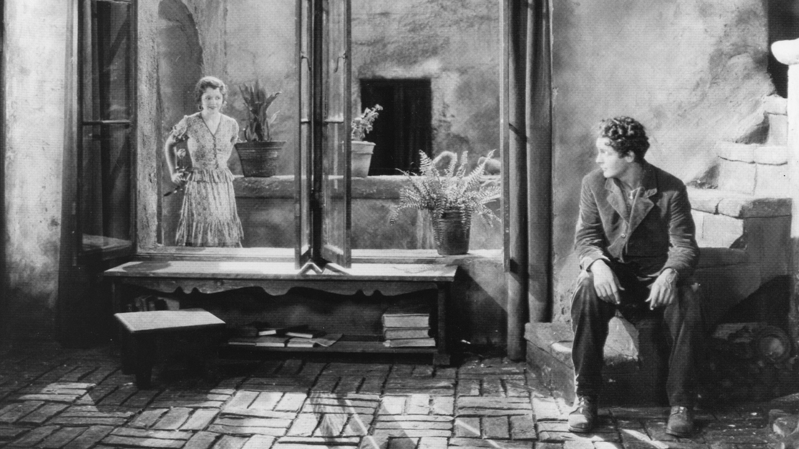 Kuvassa mies istuu alaportaalla ja katsoo naista, joka seisoo avoinna olevien isojen lasien takana.