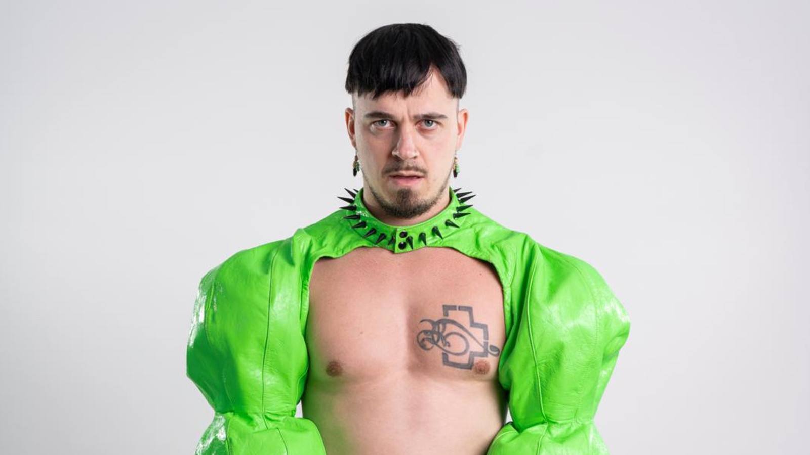 Kuvassa on Käärijä vaalean vihreässä bolerossaan puolivartalokuvassa.  Hänellä on rinta paljaana jaoikealla näkyy tatuointi ja kaulassa musta panta pystyniitteineen.