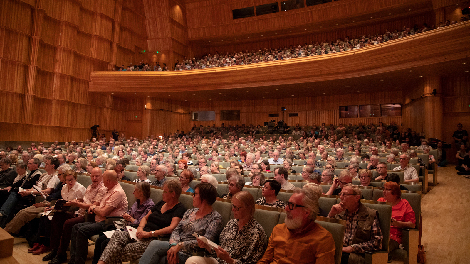 Kuvassa on yleisöä istumassa Kuhmon konserttisalissa ja paikat ovat täynnä.