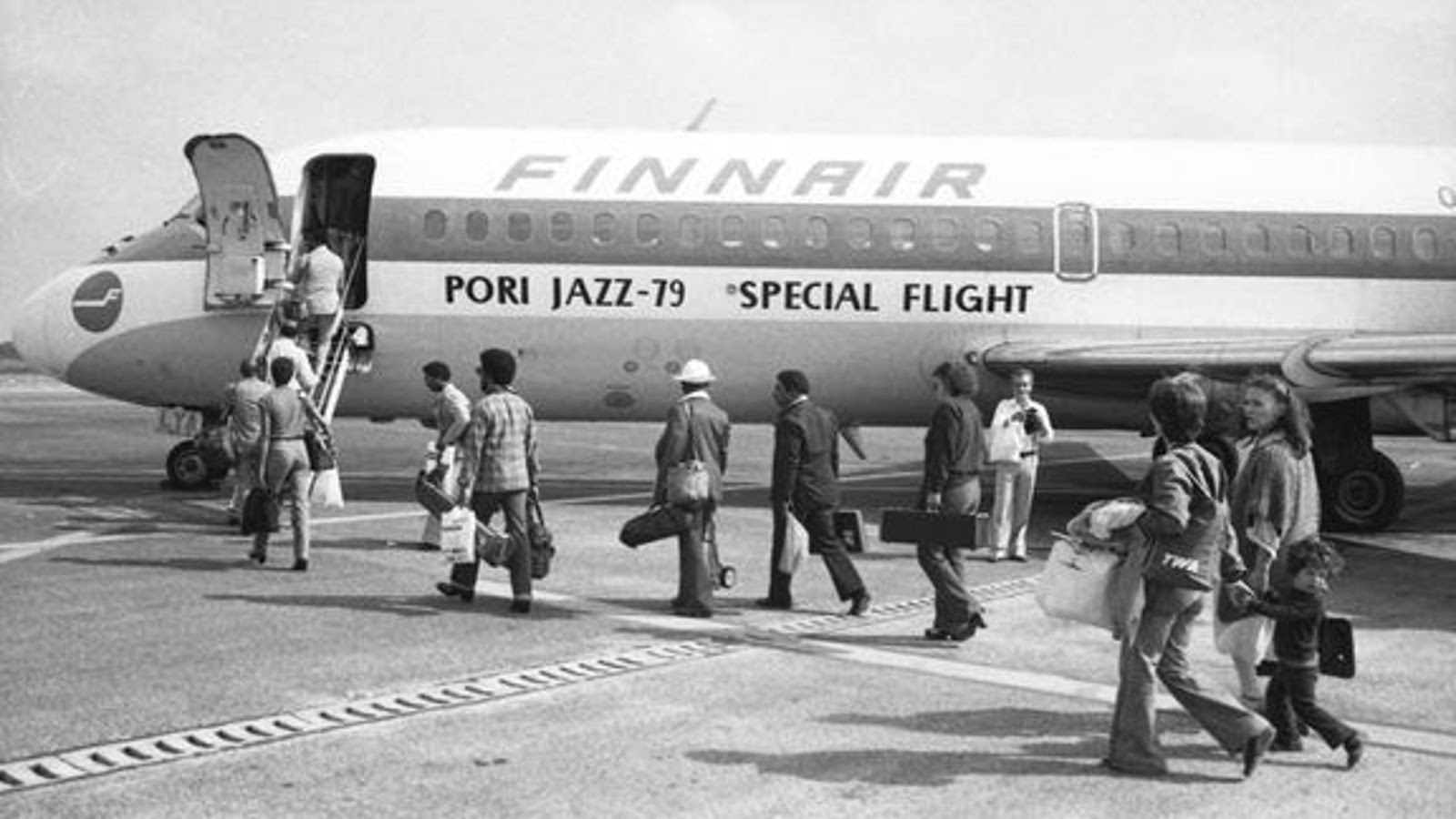 Kuvassa on Finnairin kone, johon on menossa rivissä matkustajia. Koneessa lukee Poro Jazz -79, Special Flight.  Kuva on musta-valkoinen.