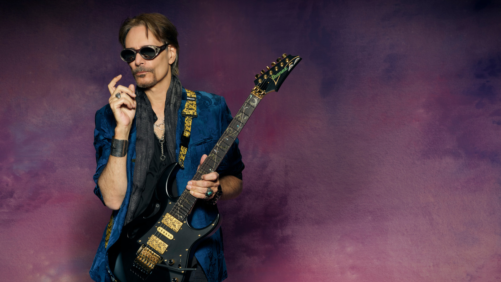 Kuvassa on Steve Vai kitara kädessään. Hänellä on tumman sininen paita päällään.  Tausta on tumman violetti ja siinä on höyryä.