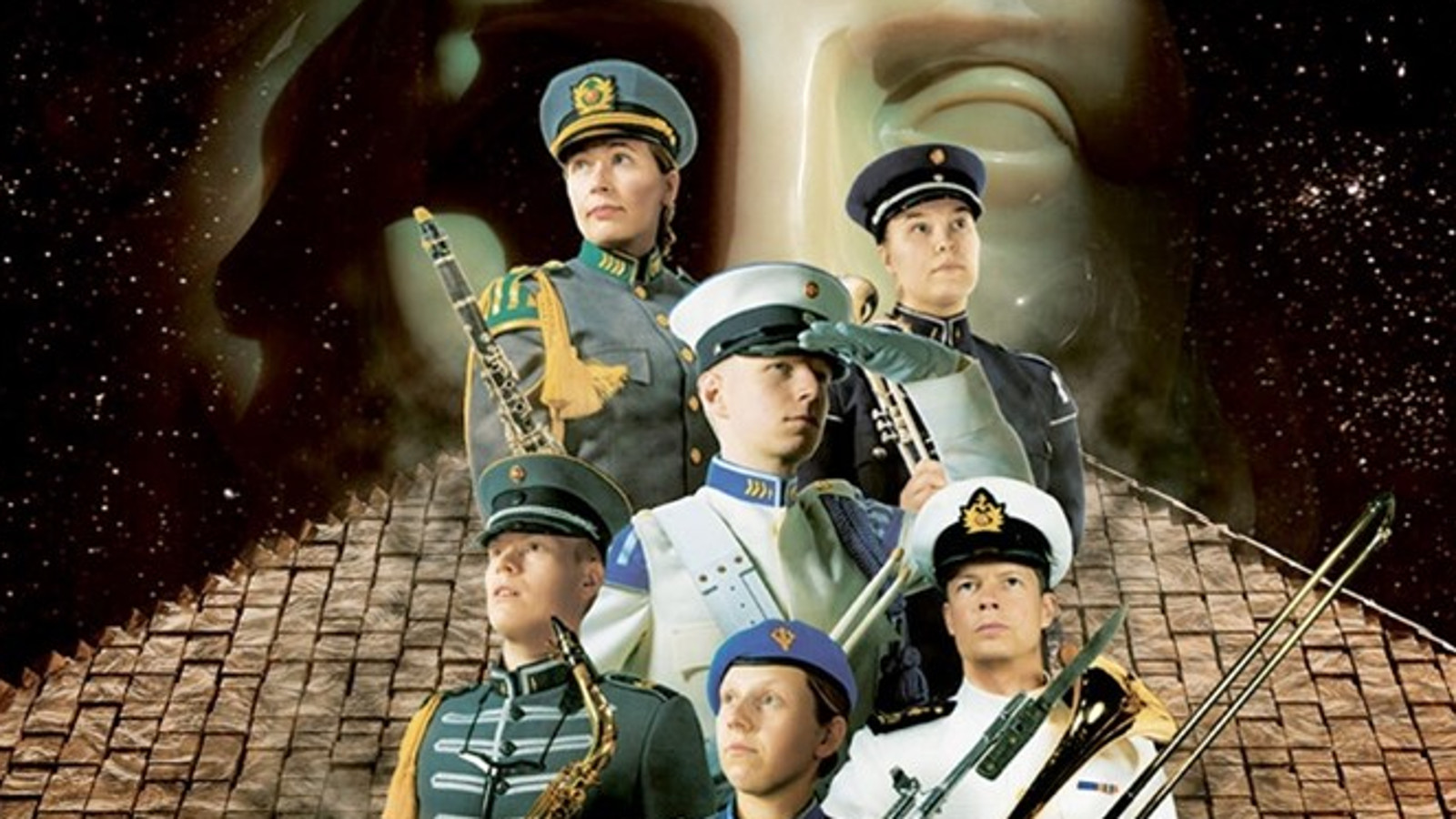 Kuvassa on seitsemän sotilassoittajaa kolmen rivin ryhmässä ja heillä on harmaita tai valkoisia takkeja sekä lakit sekä puhallinsoittimia kädessään. Taustalla on alhaalla tiilikattoa ja takana vaalean patsaan kasvot.   