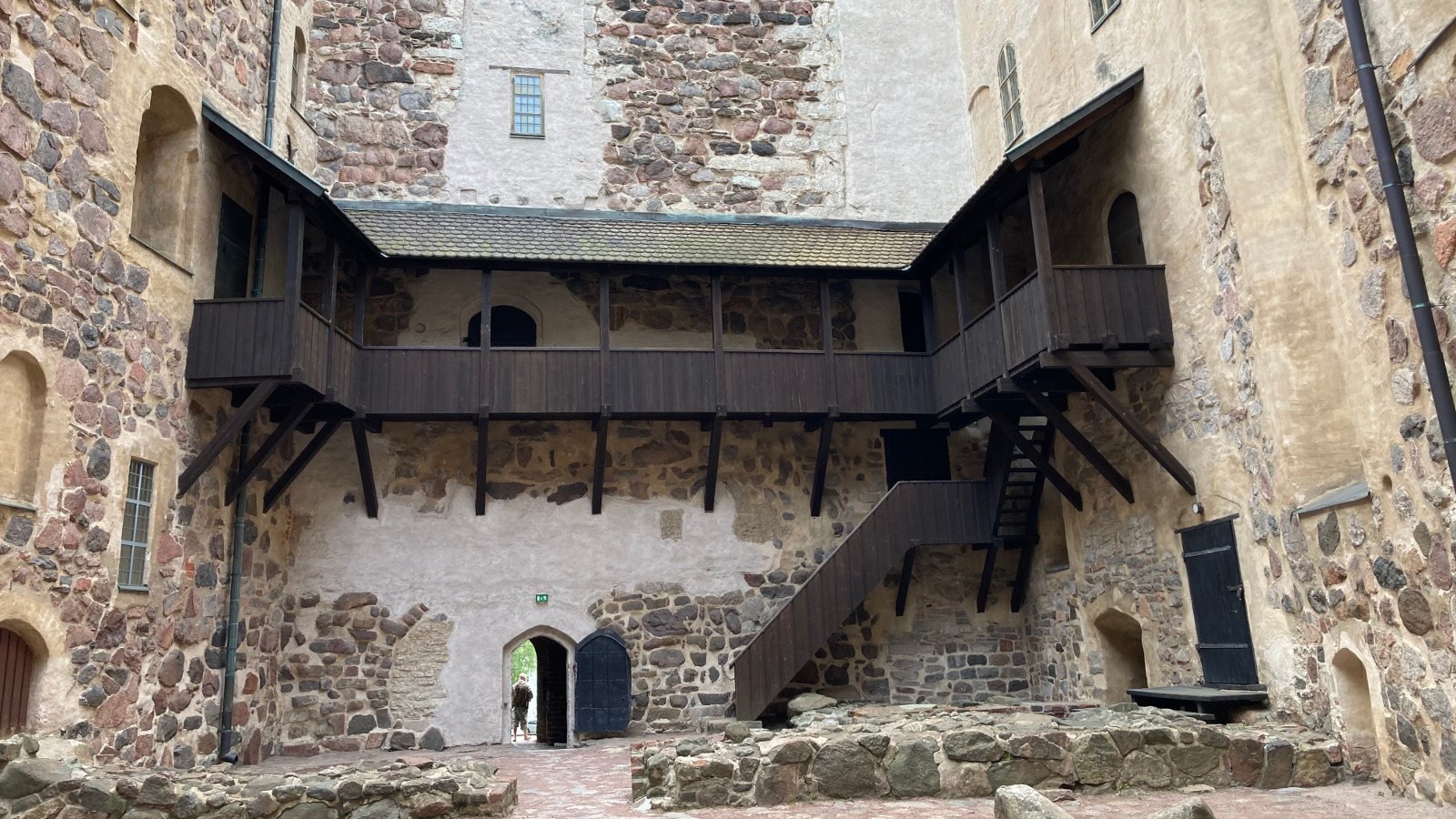 Kuvassa on Turun linnan sisäpiha ja siinä näkyviä aukkoja sekä tumma katoksellinen, puinen kulkukatos ulkokautta linnan toiseen osaan.