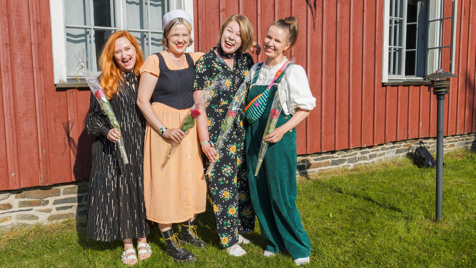 Kuvassa ovat Enkel-yhtyeen nuoret naiset Maija Pokela (vas.) Leija Lautamaja, Miia Palomäki ja Iida Savolainen ja heillä on joko pitkät puvut tai Savolaisella vihreät farkkuhaalarit. Taustalla on puna-valkoinen mökki.