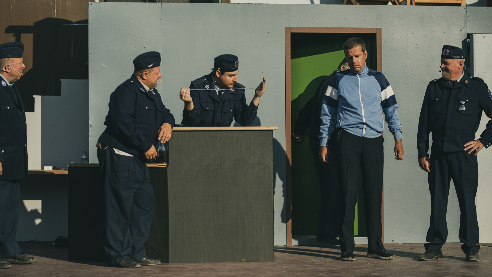 Kuvassa on kaksi poliisia oikealla ja yksi vasemmalla välissään vaalean sinisessä verkkaripuserossa olevaa pitkää miestä.