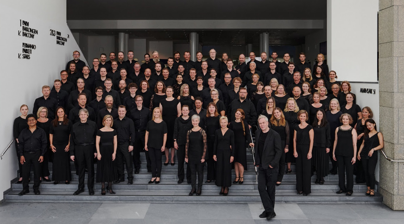 Kuvassa on Kansallisoopperan soittajat seisomassa ja heillä on mustat vaatteet.  Edessä oikealla seisoo Hannu Lintu.