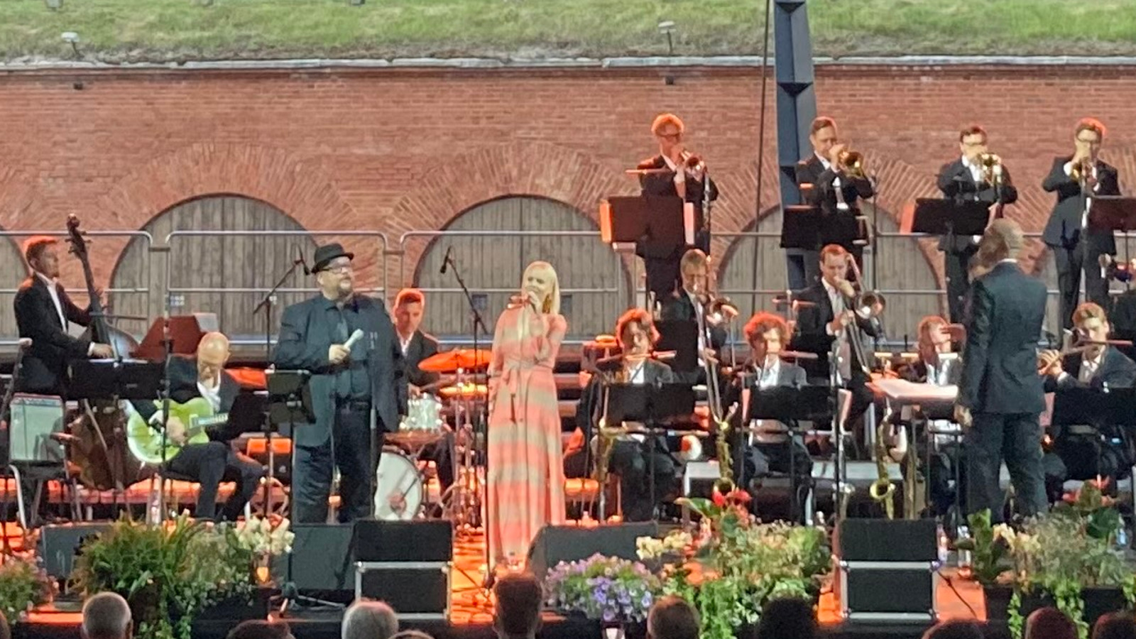 Kuvassa on orkesterin jäseniä ja keskellä laulamassa Sami Pitkämö ja Aili Ikonen. Taustalla on bastionin tiiliseinää ja siinä varastojen puisiä ovia.